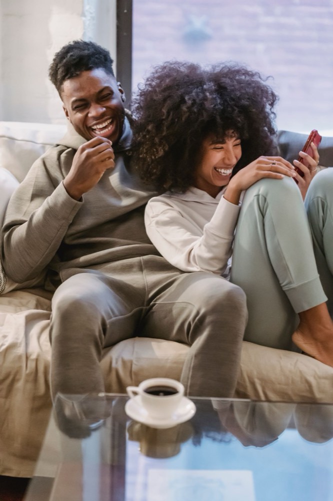 Two flatmates laughing at a phone on the sofa